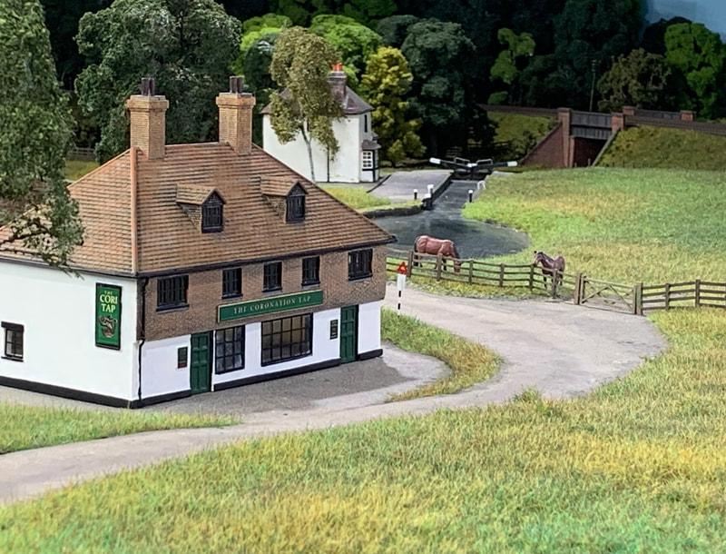 Model country pub with canal lock and railway bridge in background